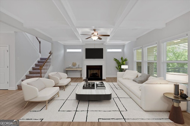 living room featuring light wood-style floors, a ceiling fan, stairs, beamed ceiling, and coffered ceiling