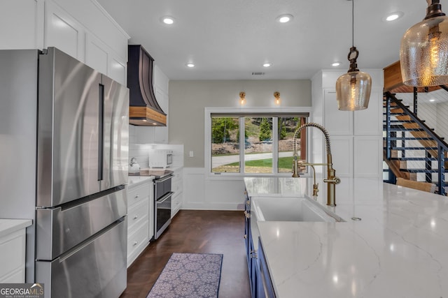 kitchen with appliances with stainless steel finishes, premium range hood, a sink, recessed lighting, and white cabinets
