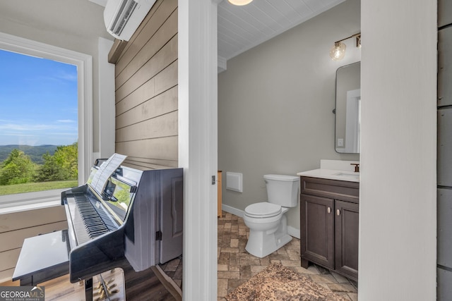 bathroom with stone finish floors, baseboards, toilet, vanity, and a wall unit AC