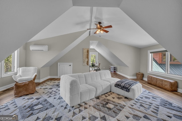 living area featuring wood finished floors, a wall mounted AC, vaulted ceiling, a ceiling fan, and baseboards