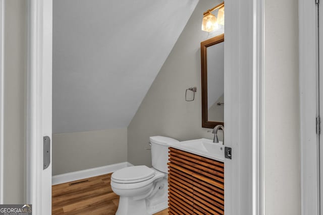 bathroom with lofted ceiling, baseboards, toilet, wood finished floors, and vanity