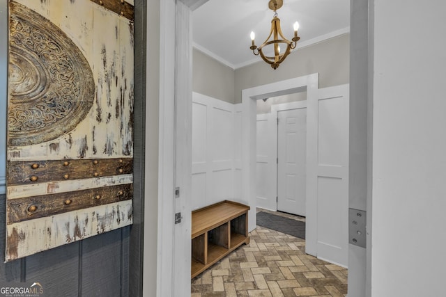mudroom with brick patterned floors, crown molding, a chandelier, and a decorative wall