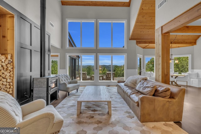living area featuring a wood stove, a high ceiling, beam ceiling, and wainscoting