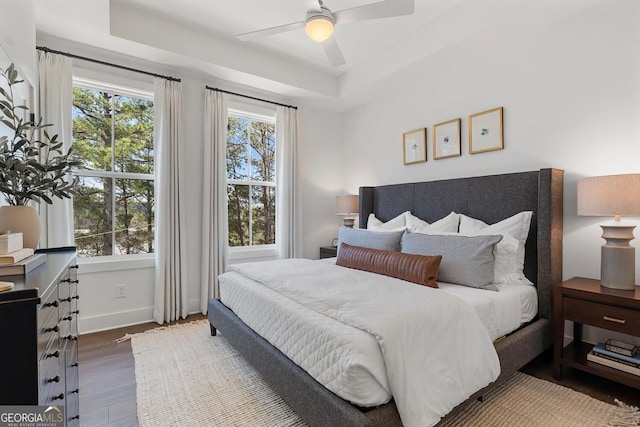 bedroom featuring a raised ceiling, wood finished floors, baseboards, and ceiling fan