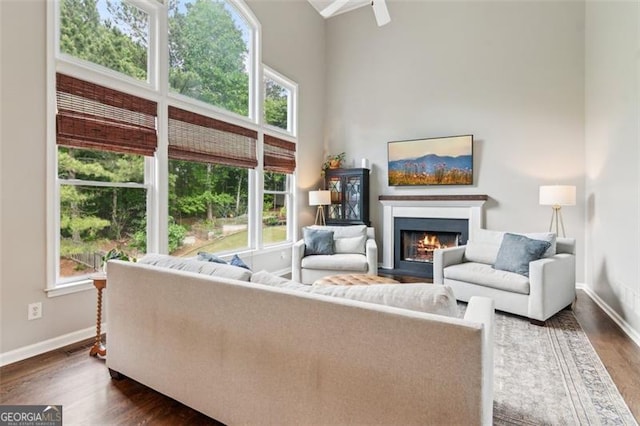 living room featuring dark wood-style floors, baseboards, a lit fireplace, and a towering ceiling
