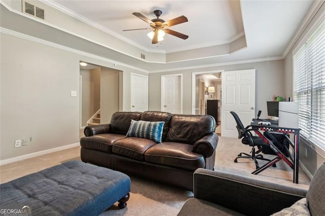 living area with carpet floors, ceiling fan, a raised ceiling, ornamental molding, and stairs