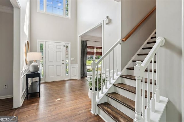 foyer with a high ceiling, healthy amount of natural light, wood finished floors, stairway, and a wainscoted wall