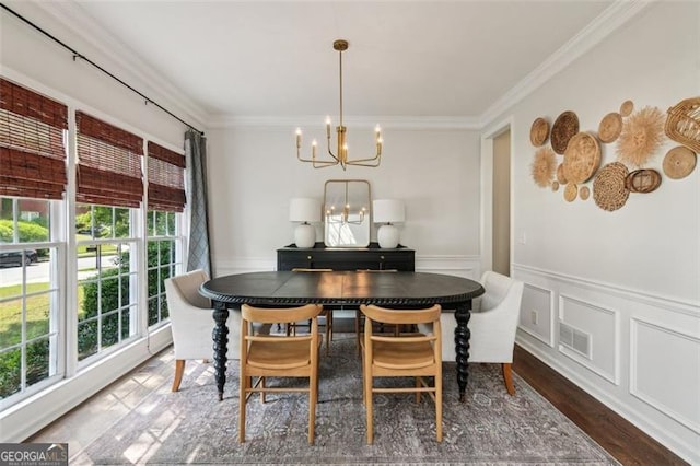 dining area featuring a chandelier, crown molding, dark wood-style flooring, wainscoting, and a decorative wall