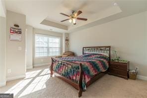 bedroom featuring a raised ceiling, carpet flooring, baseboards, and a ceiling fan