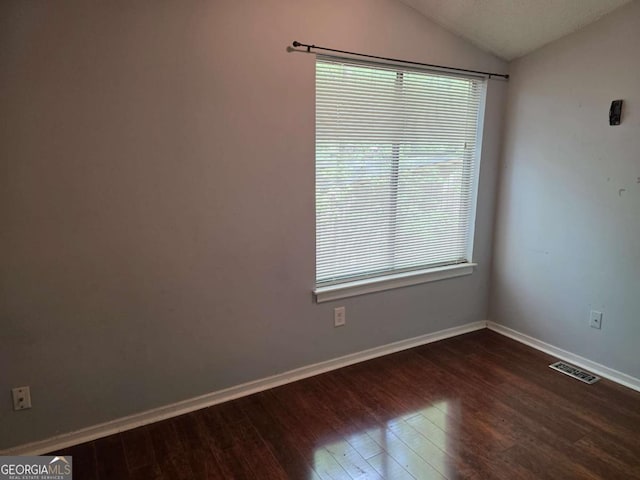 unfurnished room featuring lofted ceiling, dark wood-type flooring, plenty of natural light, and baseboards