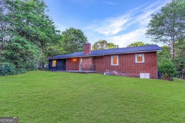 back of property featuring a chimney, a lawn, brick siding, and crawl space