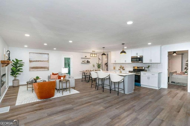 kitchen featuring stainless steel appliances, dark wood-style floors, a kitchen bar, white cabinets, and recessed lighting