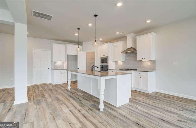 242 Linford Dr, Locust Grove, GA 30248 - kitchen featuring wall chimney exhaust hood, stainless steel appliances, tasteful backsplash, white cabinetry, and light wood-type flooring