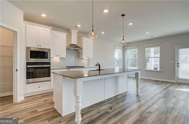 242 Linford Dr, Locust Grove, GA 30248 - kitchen with stainless steel appliances, wall chimney range hood, light wood-style floors, a center island with sink, and decorative backsplash