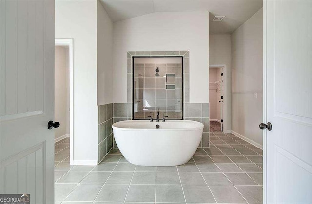 242 Linford Dr, Locust Grove, GA 30248 - bathroom with tile patterned flooring, a freestanding tub, vaulted ceiling, tile walls, and a walk in closet