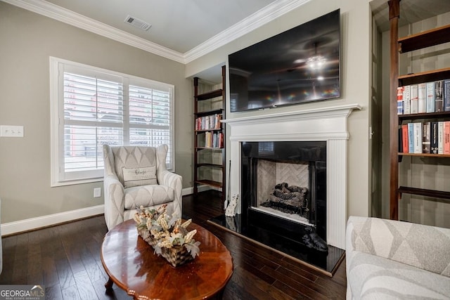 living area with a fireplace with raised hearth, crown molding, baseboards, and dark wood-style flooring