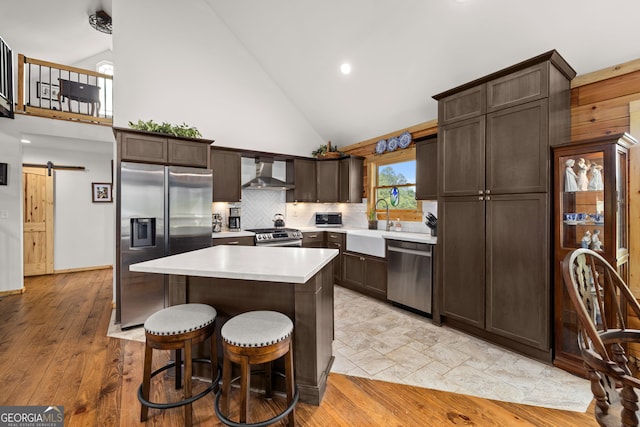 kitchen with appliances with stainless steel finishes, wall chimney exhaust hood, high vaulted ceiling, dark brown cabinets, and a barn door