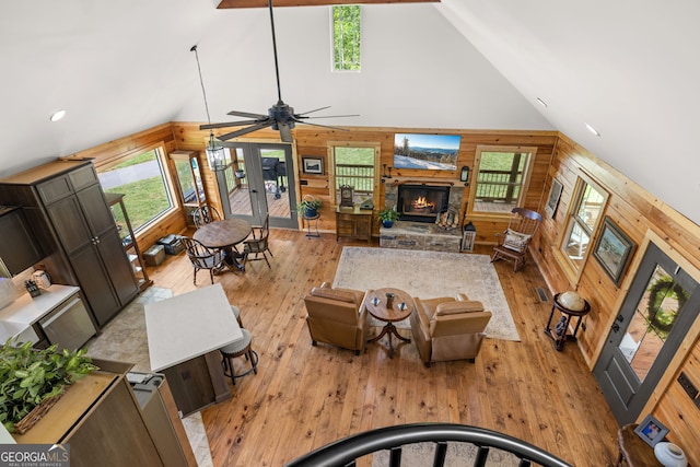 living area with wooden walls, high vaulted ceiling, healthy amount of natural light, a stone fireplace, and light wood-type flooring