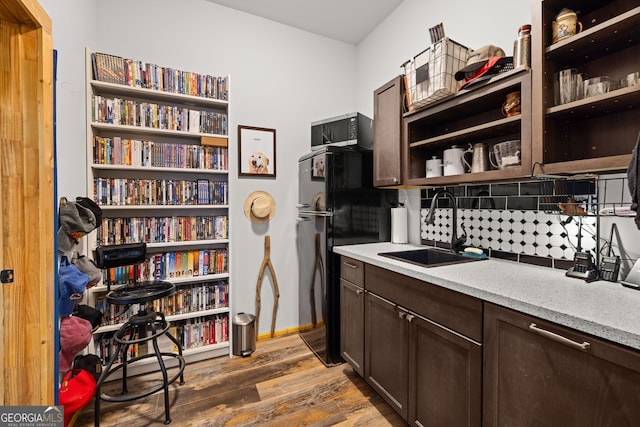 kitchen with a sink, freestanding refrigerator, open shelves, dark brown cabinetry, and wood finished floors