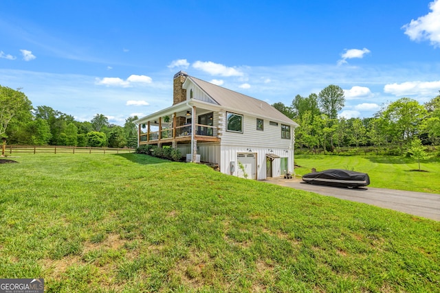 view of side of home with a chimney, an attached garage, asphalt driveway, metal roof, and a balcony