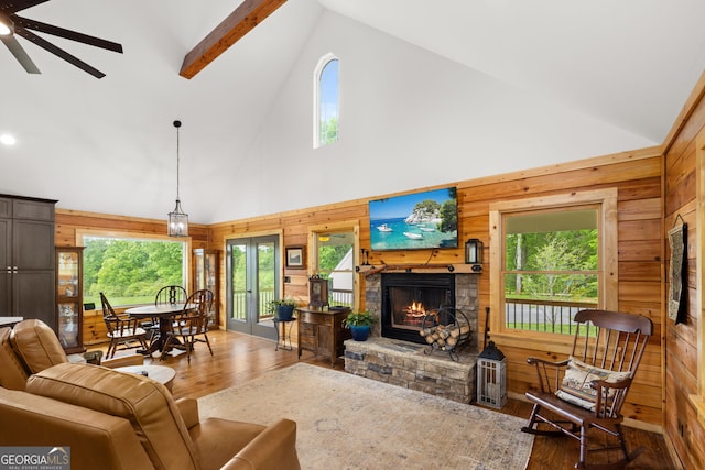 living area featuring high vaulted ceiling, wood-type flooring, wood walls, a fireplace, and a ceiling fan