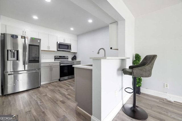 kitchen featuring appliances with stainless steel finishes, wood finished floors, light countertops, recessed lighting, and baseboards