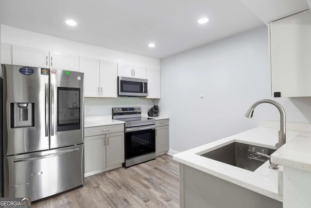 kitchen featuring stainless steel appliances, a sink, light stone countertops, light wood-style floors, and recessed lighting