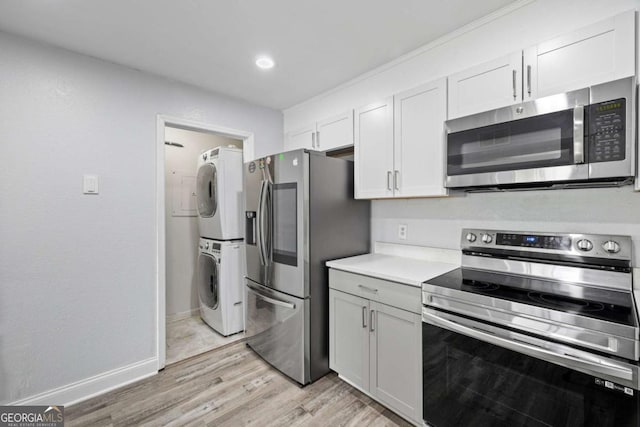 kitchen with appliances with stainless steel finishes, stacked washing machine and dryer, light countertops, light wood-type flooring, and recessed lighting