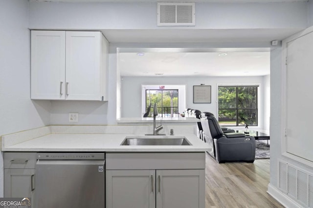 kitchen with dishwasher, a sink, light countertops, light wood-style flooring, and white cabinets