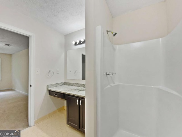 bathroom with a shower, vanity, a textured ceiling, and baseboards