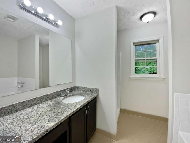 full bath with a textured ceiling, a bath, vanity, baseboards, and tile patterned floors