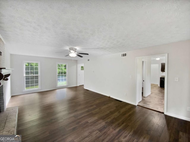 unfurnished living room with a brick fireplace, ceiling fan, dark wood finished floors, a textured ceiling, and baseboards