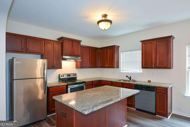 kitchen featuring stainless steel appliances, under cabinet range hood, a sink, dark wood finished floors, and a center island