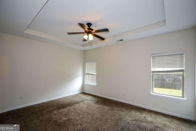 spare room featuring a raised ceiling, ceiling fan, plenty of natural light, and baseboards
