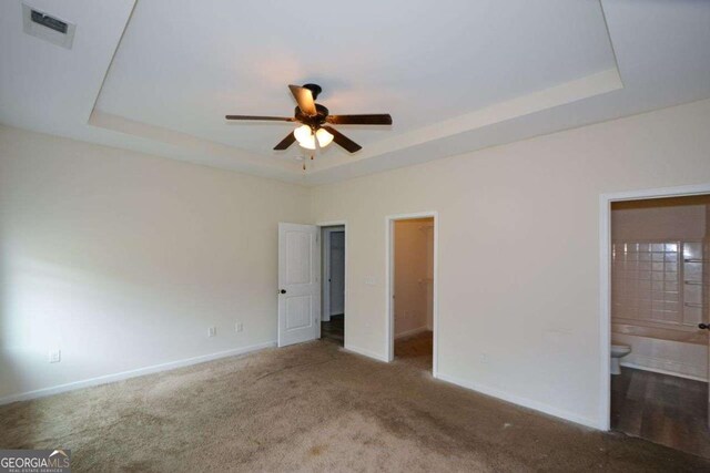 unfurnished bedroom with a tray ceiling, baseboards, a walk in closet, and carpet
