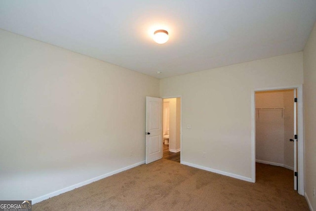 unfurnished bedroom featuring a spacious closet, carpet floors, baseboards, and a closet