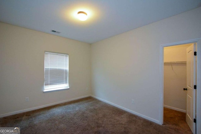 unfurnished bedroom with carpet, a spacious closet, and baseboards