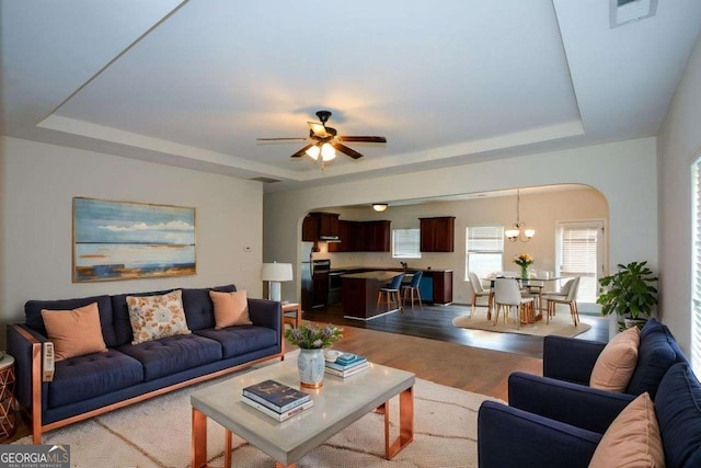 living area with arched walkways, a tray ceiling, ceiling fan, and dark wood-style flooring
