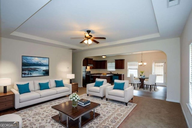 living room featuring arched walkways, a tray ceiling, and ceiling fan