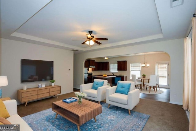 carpeted living area featuring arched walkways, a raised ceiling, ceiling fan, and baseboards