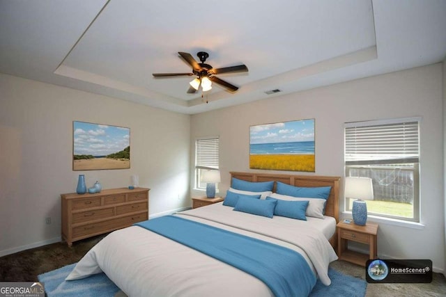 bedroom featuring a tray ceiling, multiple windows, baseboards, and a ceiling fan