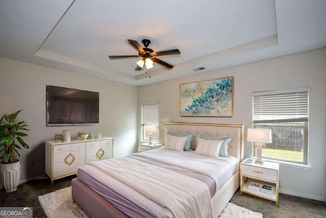 bedroom featuring a raised ceiling, carpet, baseboards, and ceiling fan