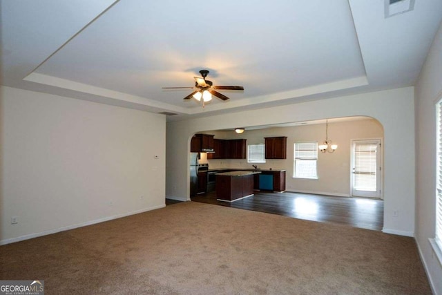 unfurnished living room featuring a tray ceiling, arched walkways, dark carpet, a ceiling fan, and baseboards
