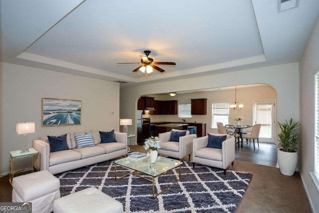 living area with arched walkways, a raised ceiling, and a ceiling fan