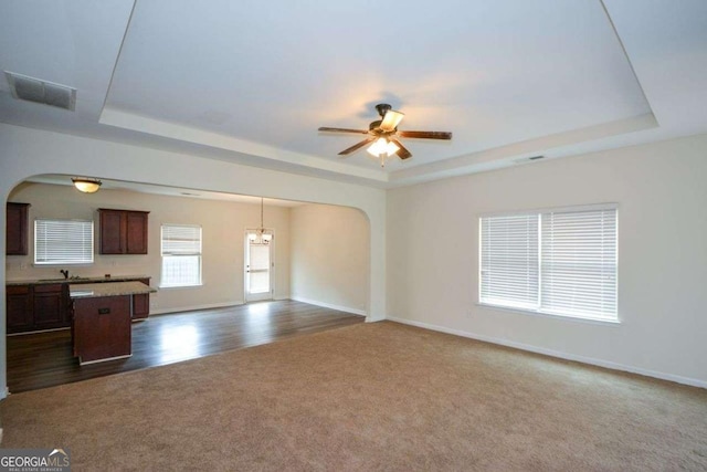 unfurnished living room with a raised ceiling, arched walkways, dark carpet, and ceiling fan