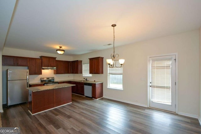 kitchen featuring stainless steel appliances, dark wood-style floors, under cabinet range hood, a chandelier, and a sink