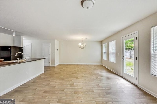 unfurnished dining area featuring a chandelier, light wood-type flooring, a sink, and baseboards