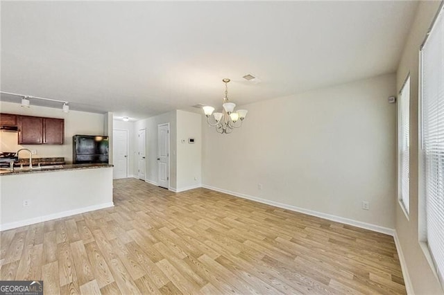 unfurnished living room with a chandelier, light wood-style floors, baseboards, and a sink