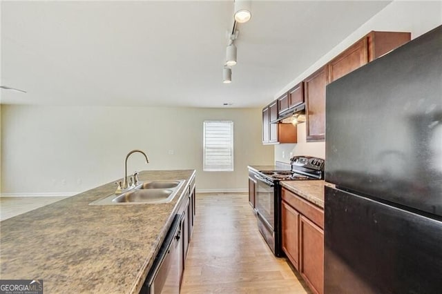 kitchen with black appliances, under cabinet range hood, a sink, light wood-style flooring, and baseboards
