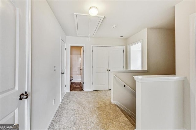 hall with attic access, carpet floors, baseboards, and an upstairs landing